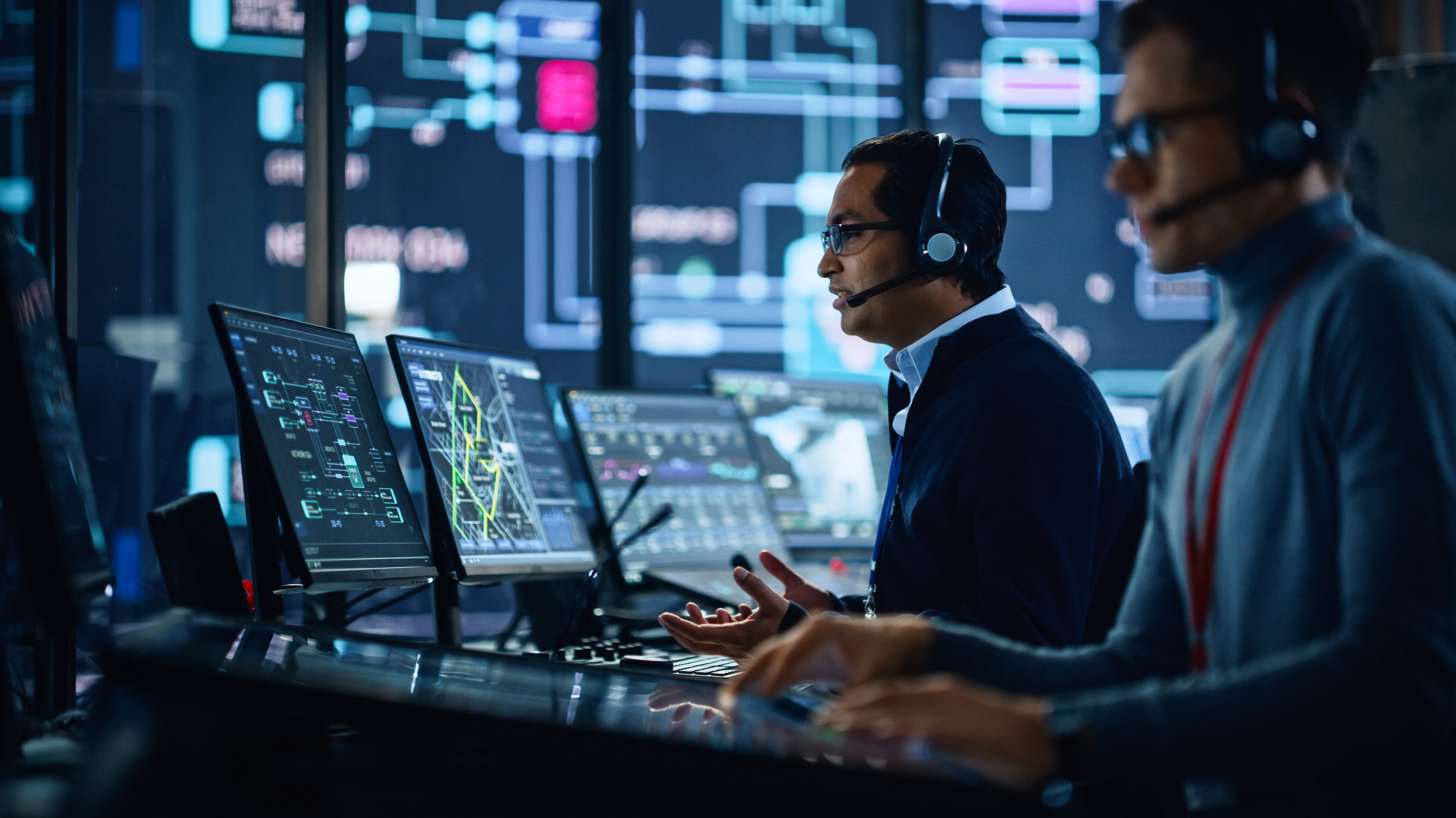 two men with headsets reviewing multiple screens with security data